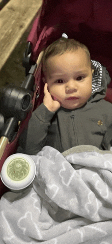 a baby is sitting in a stroller with a blanket and a jar of cream