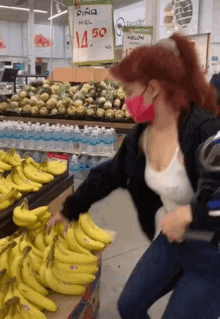 a woman wearing a red mask reaches for a bunch of bananas in front of a sign that says pina miel