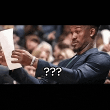 a man in a suit is holding a piece of paper and says " ? "