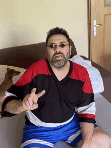 a man with a beard and glasses is sitting on a bed giving a peace sign