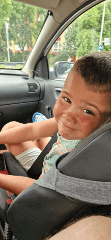 a young boy sits in a car seat and smiles