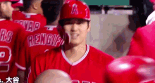 a baseball player wearing a red uniform and a red helmet is standing in the dugout with his teammates .