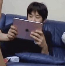 a man is sitting on a blue couch holding an apple tablet