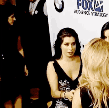 a woman in a black dress is talking to another woman in front of a fox sign .