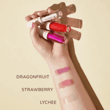 a hand holding three lip glosses with dragonfruit strawberry and lychee