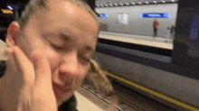 a woman sitting at a train station with her eyes closed and her hands on her face