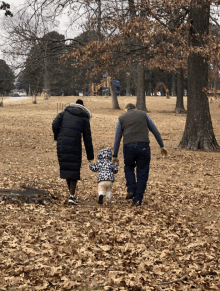 a man and woman holding a child 's hand in a park