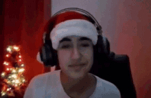 a young boy wearing headphones and a santa hat is sitting in front of a christmas tree .