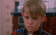 a young boy in a plaid shirt is making a face .