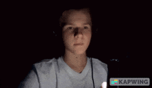 a young man is using a cell phone in the dark and the word kapwing is on the bottom right