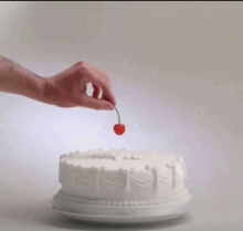 a hand is putting a cherry on top of a cake