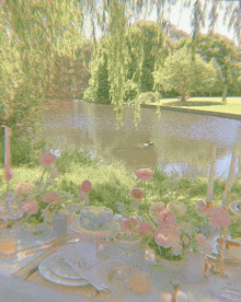 a table with plates candles and flowers in front of a pond