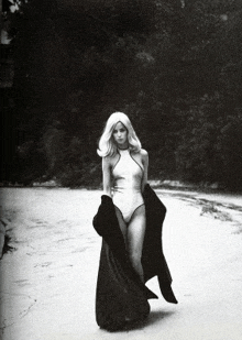 a black and white photo of a woman in a bathing suit holding a black coat