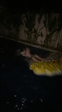 a person is floating on a yellow raft in a pool at night