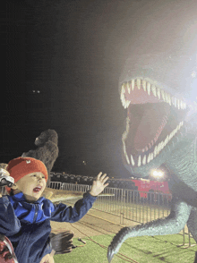 a little boy stands in front of a giant dinosaur statue