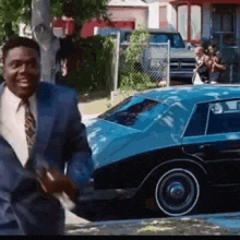 a man in a suit and tie is smiling in front of a blue car .