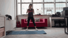 a woman stands on a yoga mat in front of a red couch with a sign on the wall that says no smoking