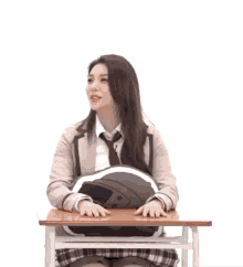 a girl in a school uniform sits at a desk with a pillow in her lap and a foreign language behind her