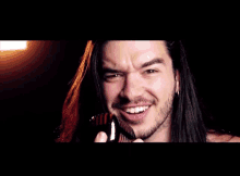 a man with long hair and a beard is smiling and holding a comb to his face