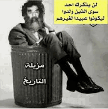 a man with a beard is sitting in a trash can with arabic writing on it .