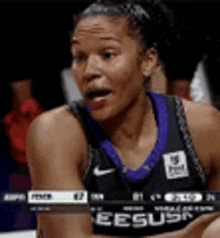 a female basketball player in a black and purple jersey is sitting on the court .