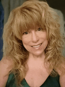 a woman with blonde curly hair and bangs smiles for the camera