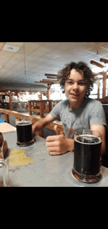 a boy sitting at a table with two glasses of beer in front of him