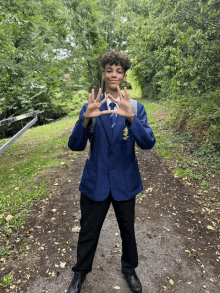 a young man in a blue jacket and black pants stands on a dirt path