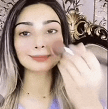 a woman is applying makeup to her face with a brush and smiling .