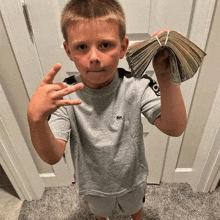 a young boy in a grey lacoste shirt holds a stack of money