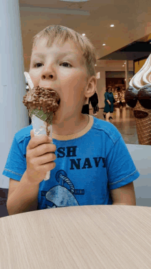 a young boy wearing a blue shirt that says navy is eating a chocolate ice cream cone