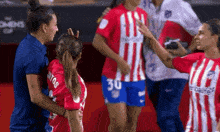 a woman in a red and white striped shirt with the number 30 on it is talking to another woman on a soccer field .