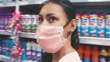 a woman wearing a pink face mask stands in front of a shelf with bottles of tide