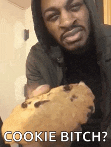 a man in a hoodie is holding a chocolate chip cookie and says cookie bitch .