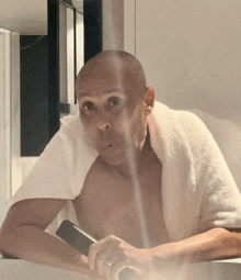 a shirtless man with a towel around his neck is holding a cell phone