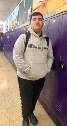 a man wearing a grey champion hoodie is standing in a hallway