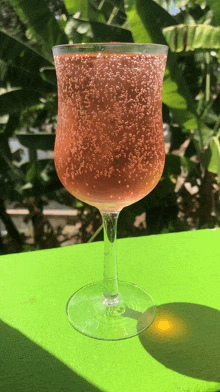 a wine glass filled with a pink drink on a green table