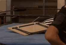 a man in a black shirt is sitting in a wrestling ring with a table in front of him