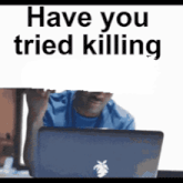 a man is sitting in front of a laptop computer with a sign that says have you tried killing