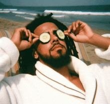 a man in a white robe is laying on a beach with cucumber slices on his eyes