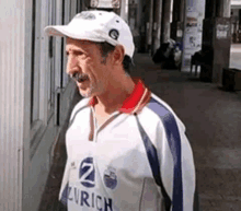 a man wearing a zurich shirt and hat is walking down a sidewalk