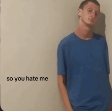 a man in a blue shirt is standing in front of a white wall with the words so you hate me written on it