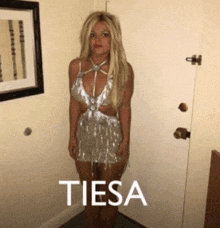 a woman in a silver dress is standing next to a door with the word tiesa written on it