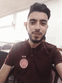 a man with a beard wears a maroon shirt with a pink emblem that says city rugby club