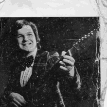 a man in a suit and bow tie is holding a guitar and smiling