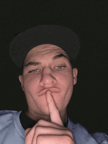 a young man wearing a hat is making a funny face with his finger on his mouth