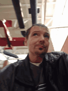 a man in a black leather jacket looks up at the ceiling