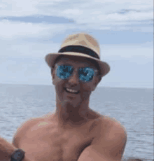 a shirtless man wearing a hat and sunglasses is taking a selfie in the ocean .