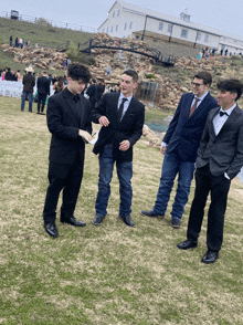 a group of men are standing in a grassy field with a white building in the background