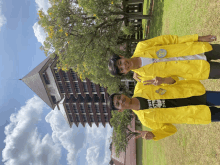 two young men wearing yellow jackets pose for a picture in front of a tall building